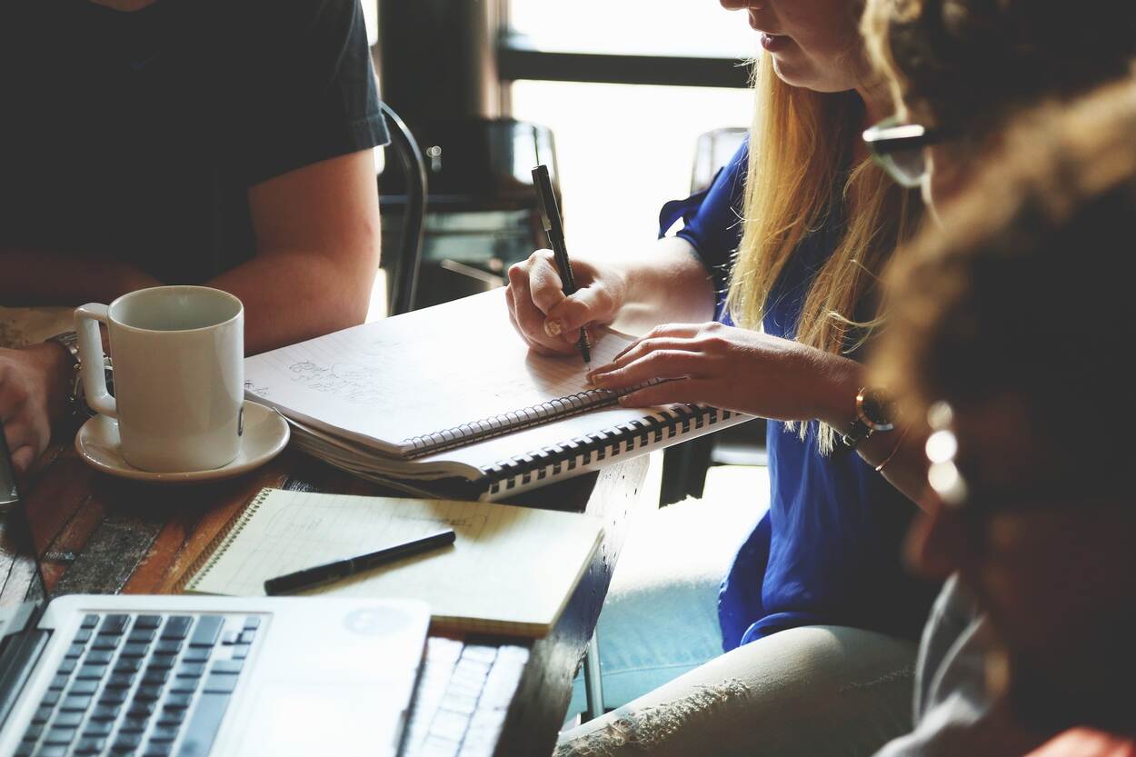 Verschillende mensen overleggen aan een tafel met een aantal documenten op de tafel, een laptop en een kopje koffie